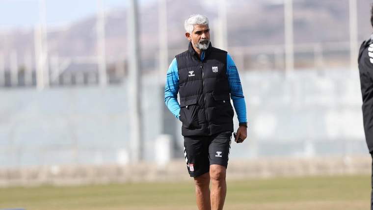 Spor sahasında siyah yelek ve mavi üst giyen sakallı bir kişi yürürken görülüyor.