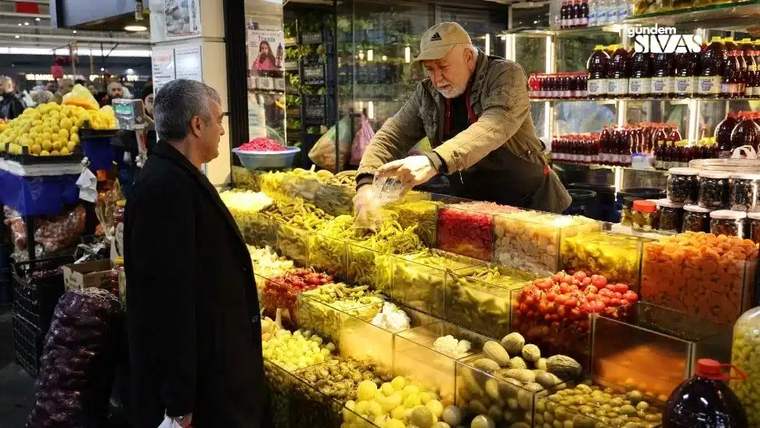 Kapalı çarşı tezgâhında kavanozlarda turşular sergilenirken iki kişi tezgâhın önünde duruyor.