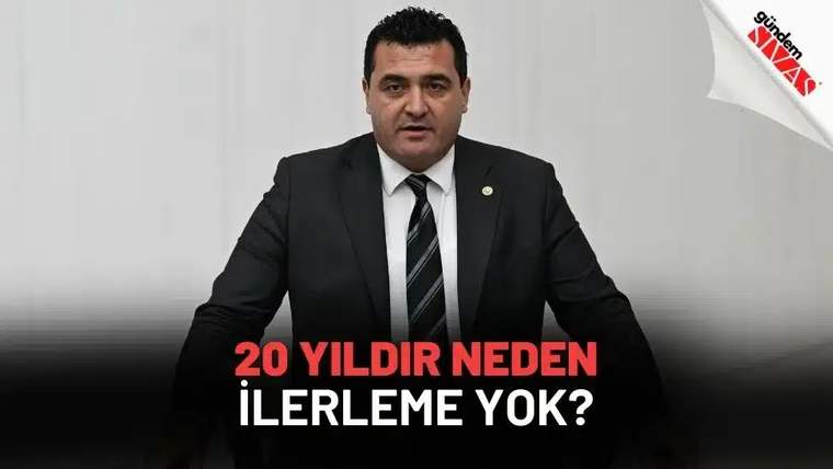 Siyah takım elbiseli bir kişi, beyaz arka plan önünde oturuyor; altta soru biçiminde yazı yer alıyor.