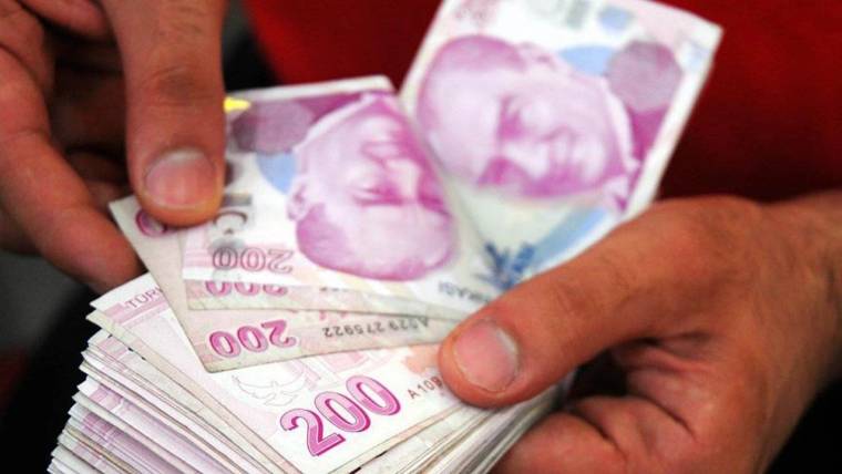 Eller, üstte 200 liralık banknotların bulunduğu bir Türk lirası para destesini tutuyor.