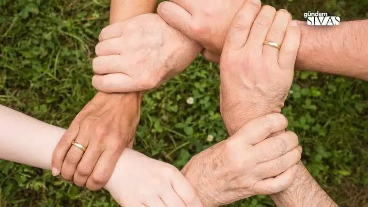 Çimlerin üzerinde dört kişinin elleri, birbirlerinin bileklerini tutarak dairesel bir düzen oluşturuyor.