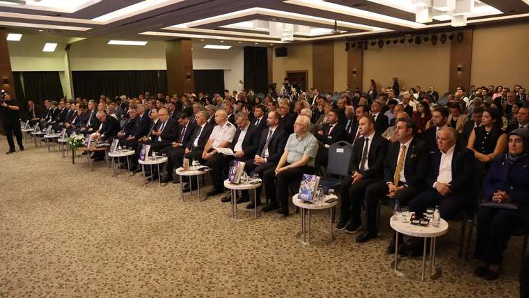 Bir etkinlikte oturan kalabalık bir grup insan, sahneye doğru bakıyor.