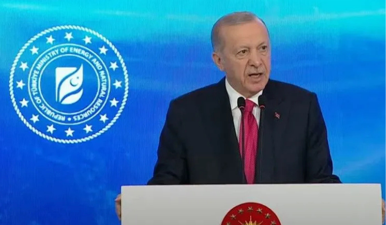 Mavi zemin önünde, üzerinde enerji bakanlığı amblemi bulunan kürsüde konuşan bir kişi