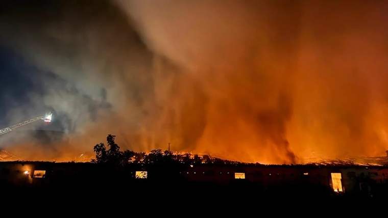 Gece karanlığında ağaçların arkasında uzanan yangın hattı, yoğun turuncu duman ve alevlerle görülüyor.