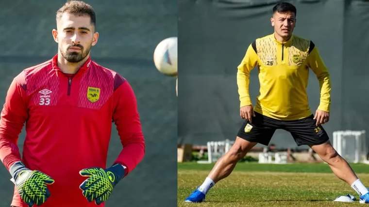 Kırmızı kaleci forması giyen bir futbolcu ile sarı formalı bir futbolcu antrenman sahasında görülüyor.