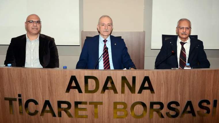 ADANA TİCARET BORSASI yazılı kürsünün arkasında üç erkek yan yana oturuyor.