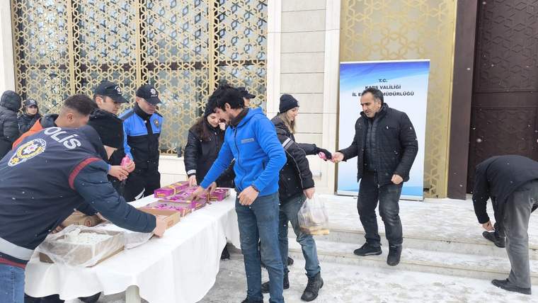 Süslemeli bir bina girişinin önünde, masadaki kutuları dağıtan ve alan insanlar görülüyor.