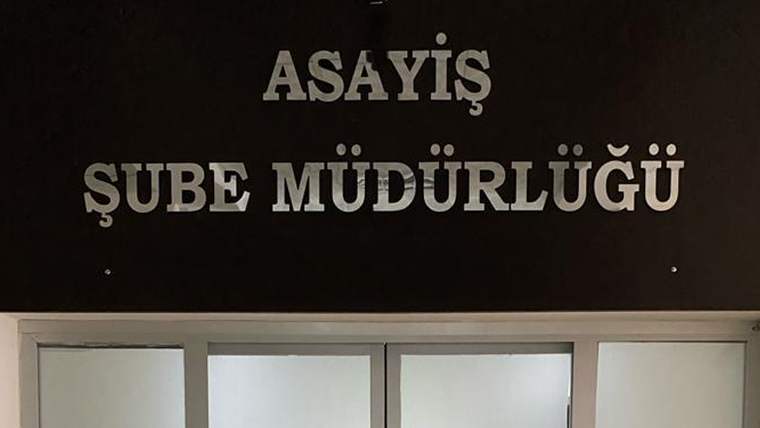 Üzerinde “ASAYİŞ ŞUBE MÜDÜRLÜĞÜ” yazan koyu renkli tabela ve altında camlı giriş kapıları görülüyor.