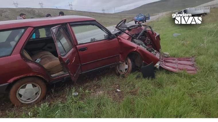 Çimlik alanda duran kırmızı otomobilin ön bölümü ağır hasar görmüş, kapıları açık.