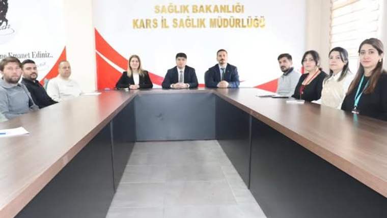 Kars İl Sağlık Müdürlüğü yazılı salonda, U düzenindeki masa çevresinde oturan kişiler görülüyor.