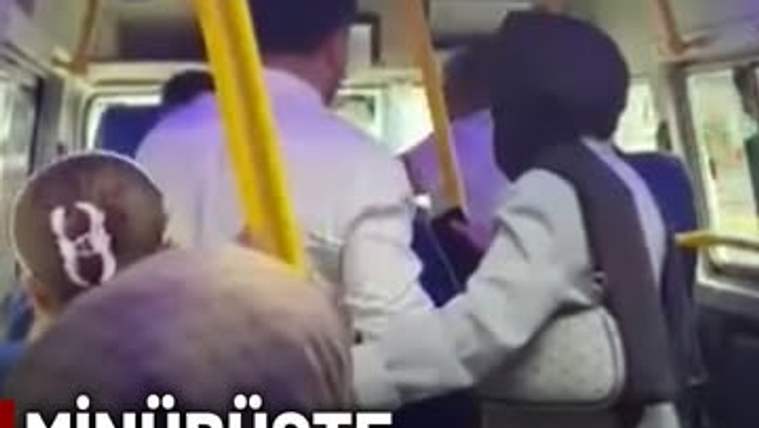 Minibüs içinde yolcular, direksiyonda oturan şoföre bakıyor. Bir kadın, şoförün yanındaki tutamaklardan birine tutunmuş.