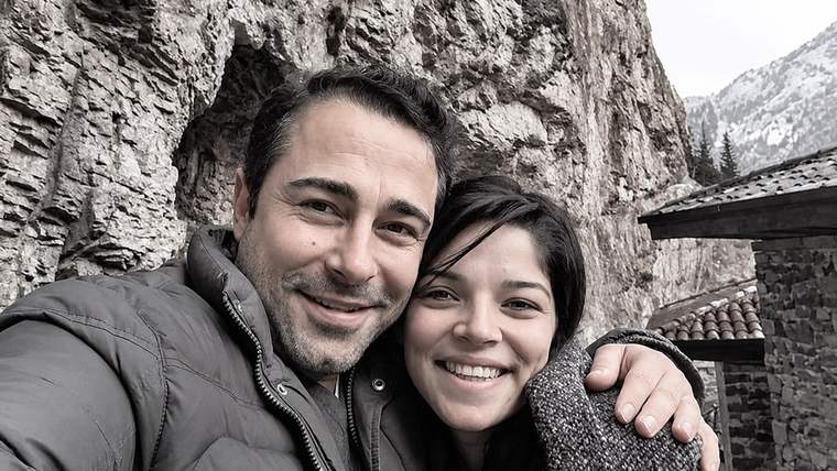 Kayalık dağ yamacının önünde, bir erkek ve genç kadın yan yana gülümseyerek selfie çekiyor.