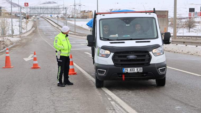 Yolda durdurulmuş bir beyaz minibüs, yanında trafik polisi ve koni var.