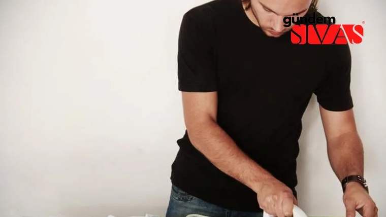 Koyu renk tişört giymiş bir erkek, ütü yapıyor.