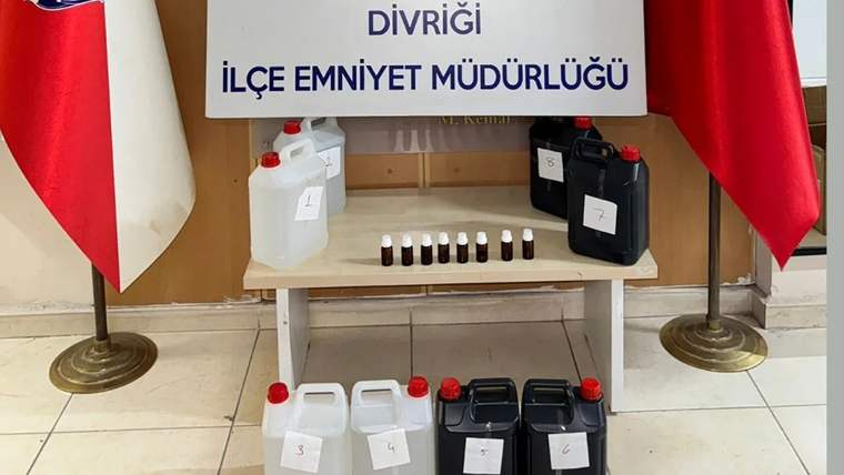 “Divriği İlçe Emniyet Müdürlüğü” yazılı pano önünde, etiketli bidonlar ve küçük şişeler sergileniyor.