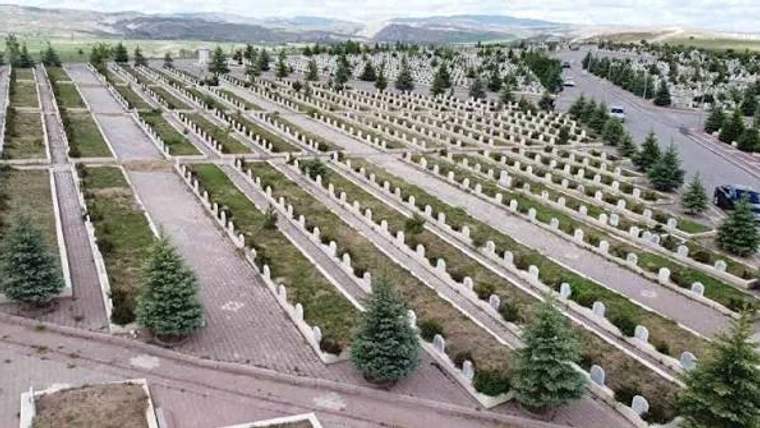 Bir mezarlık alanında sıralı mezar taşları ve ağaçlar görünmekte.