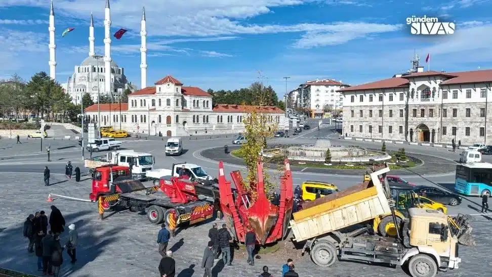 Bir ağaç, kamyonet ve iş makinesi ile kaldırılıyor; arka planda cami ve binalar görünüyor.