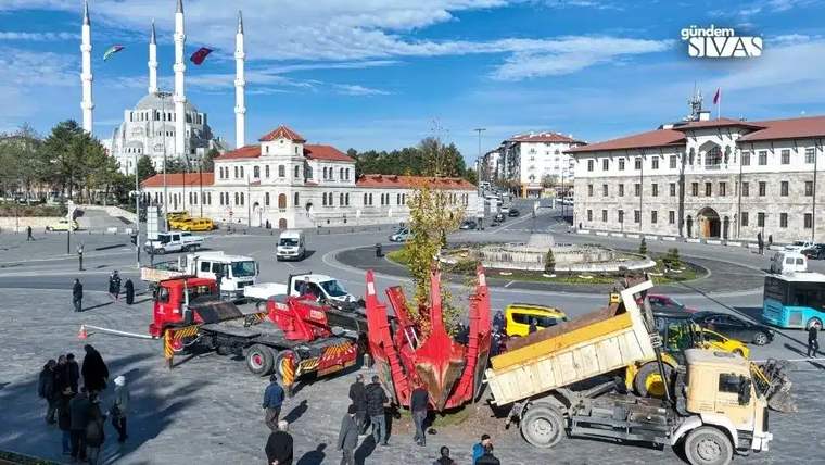 Bir ağaç, kamyonet ve iş makinesi ile kaldırılıyor; arka planda cami ve binalar görünüyor.