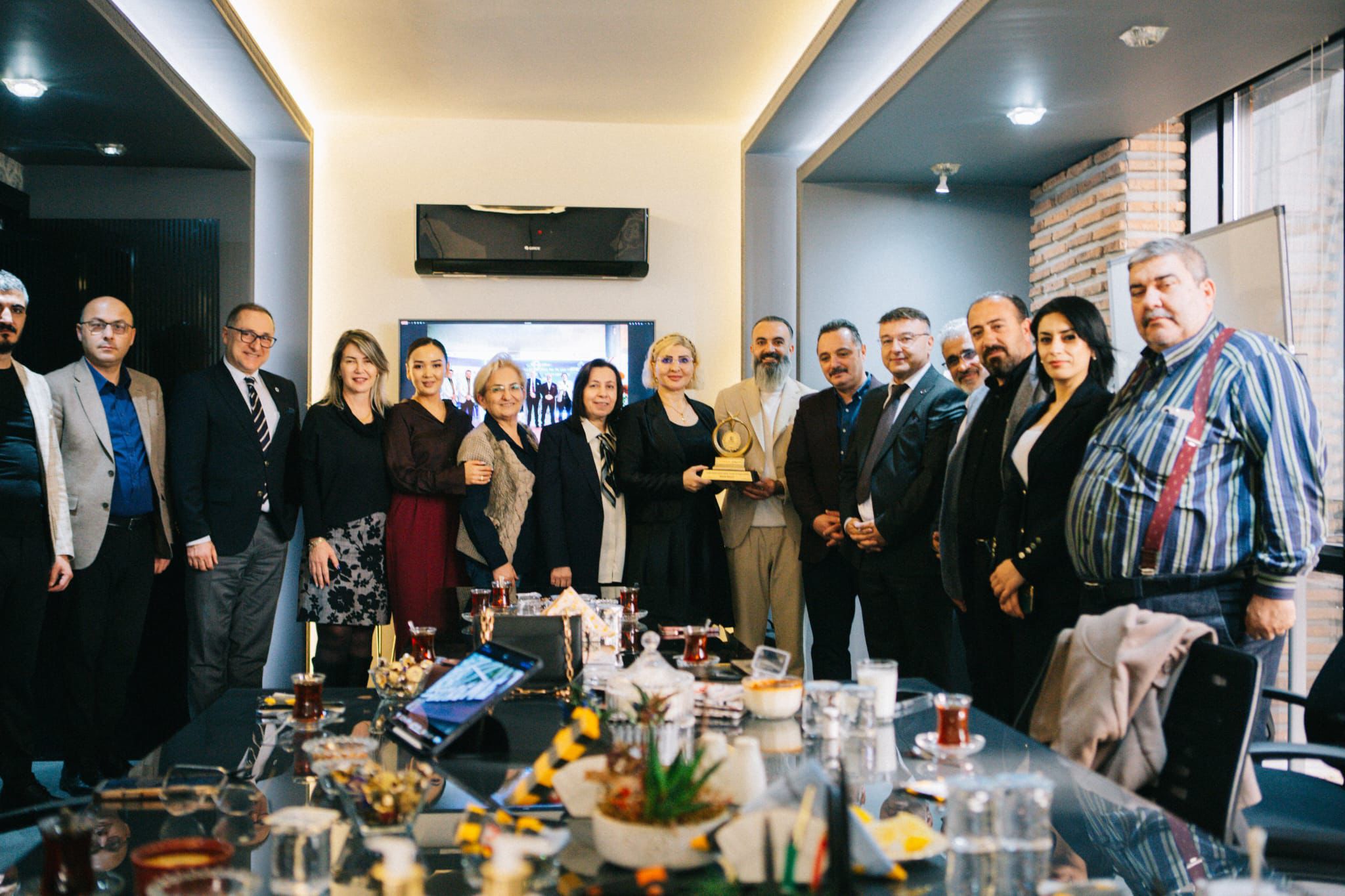 Bir grup insan, masanın etrafında durarak ödül töreninde poz veriyor.