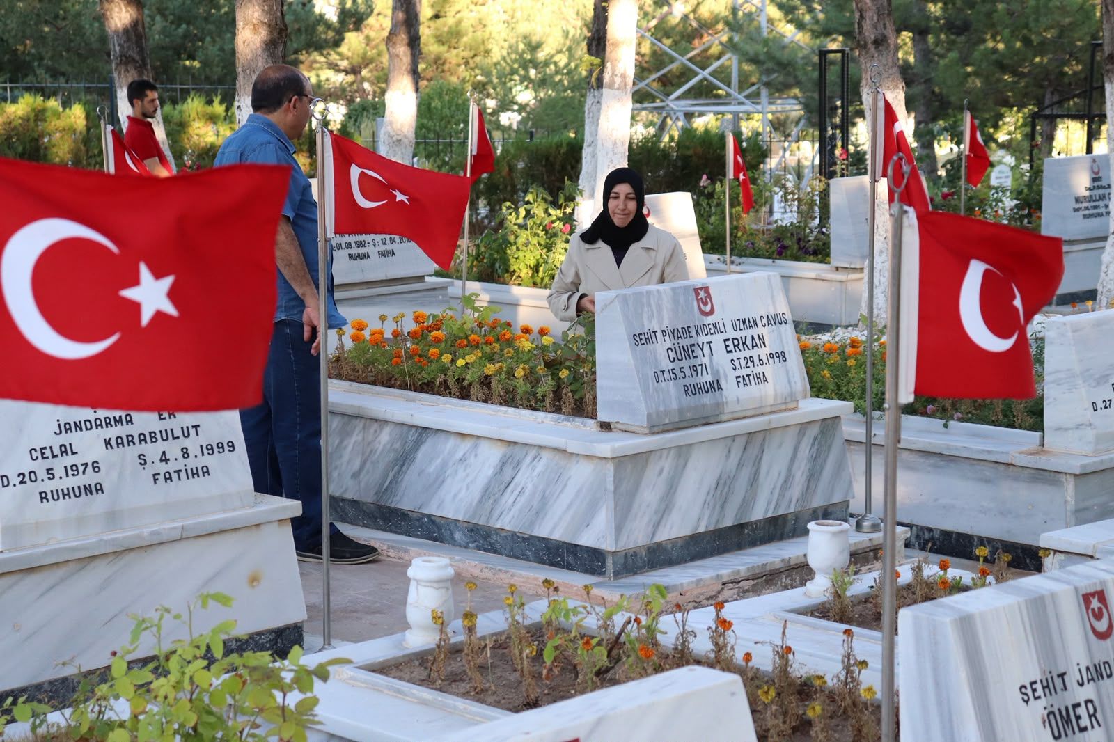 Türk bayrakları arasındaki şehitlikte, başörtülü bir kadın üzerinde yazılar bulunan pankartı tutuyor.