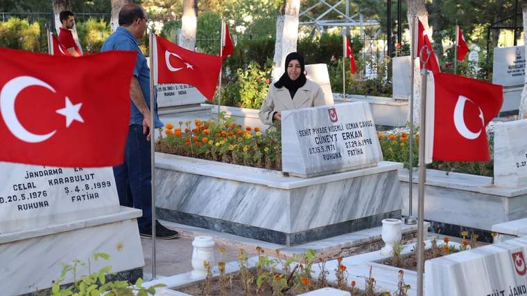 Türk bayrakları arasındaki şehitlikte, başörtülü bir kadın üzerinde yazılar bulunan pankartı tutuyor.