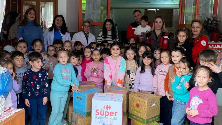 Ramazan bağışı yapan çocuklar, kutuların önünde gülümseyerek poz veriyor.