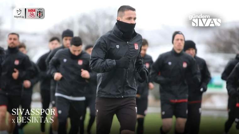 Siyah antrenman kıyafetli futbolcular açık alanda koşu yaparken öndeki oyuncu yüzünü boyunlukla kapatıyor.