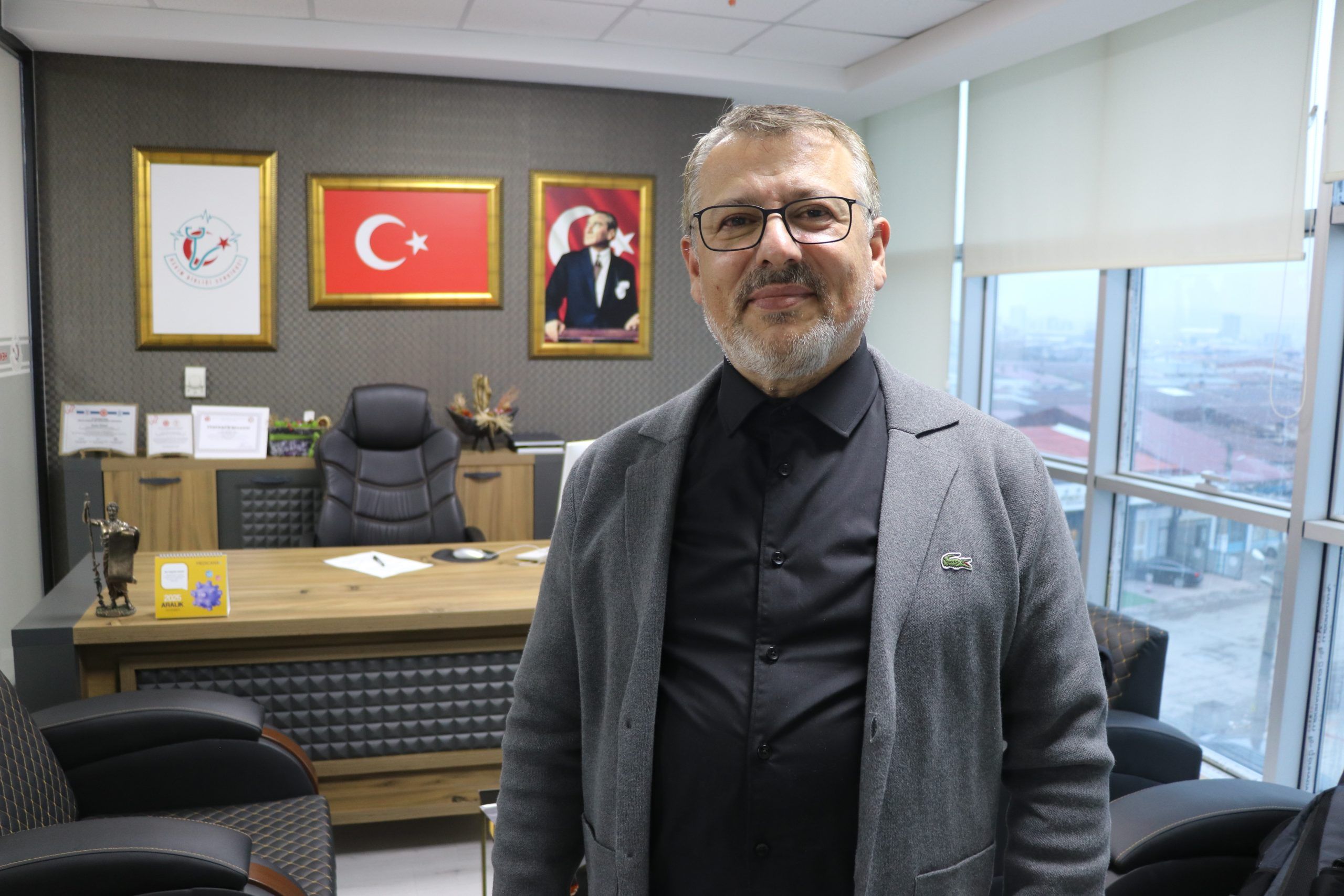 Bir ofiste, arka planda Türk bayrağı ve Atatürk portresi bulunan bir masa önünde duran bir kişi.