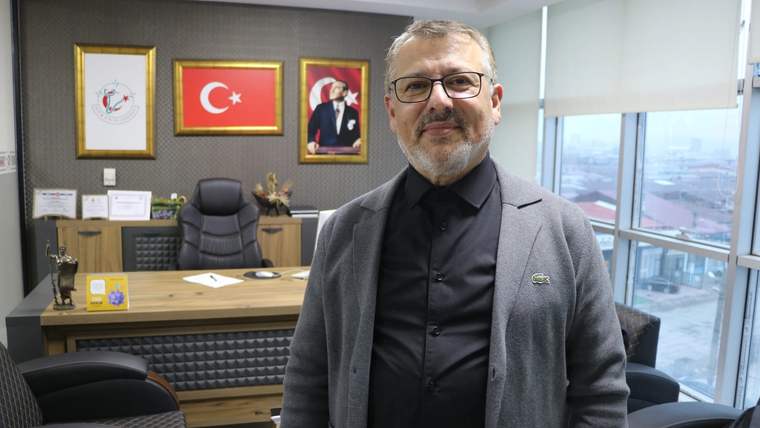 Bir ofiste, arka planda Türk bayrağı ve Atatürk portresi bulunan bir masa önünde duran bir kişi.
