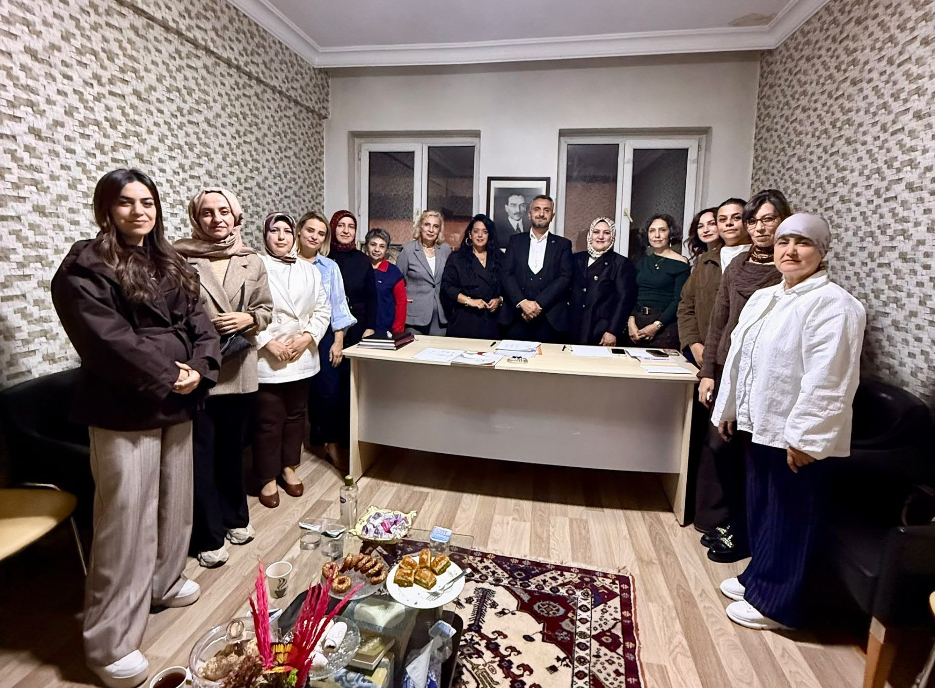 Masa çevresinde duran kadın ve erkeklerden oluşan grup, iç mekânda birlikte poz veriyor.