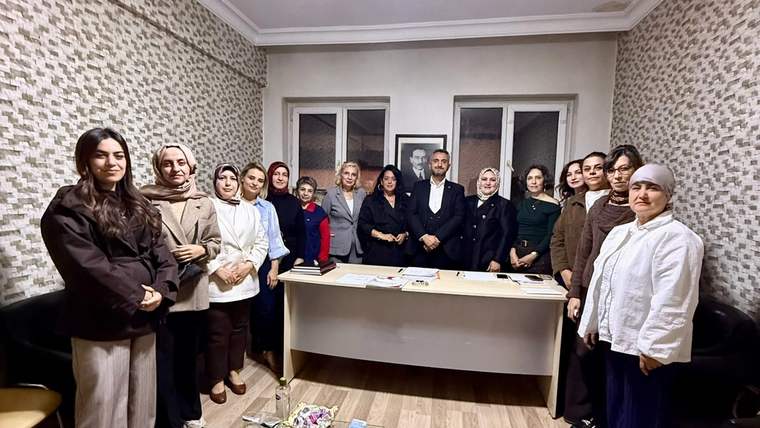 Masa çevresinde duran kadın ve erkeklerden oluşan grup, iç mekânda birlikte poz veriyor.