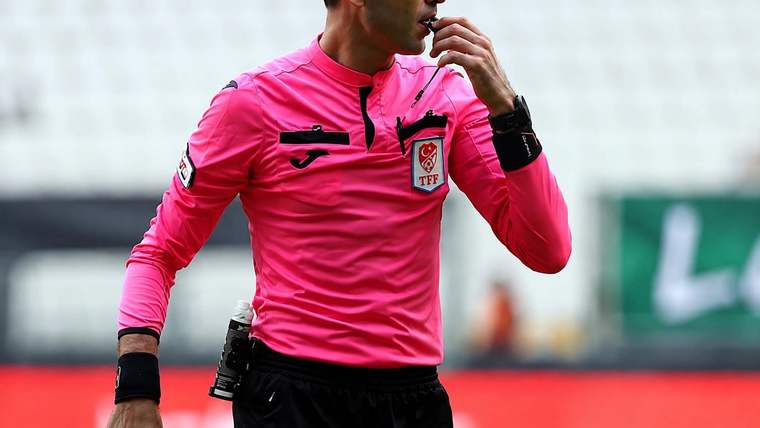 Pembe forma giyen bir futbol hakemi, düdüğünü ağzına götürürken saha içinde görülüyor.