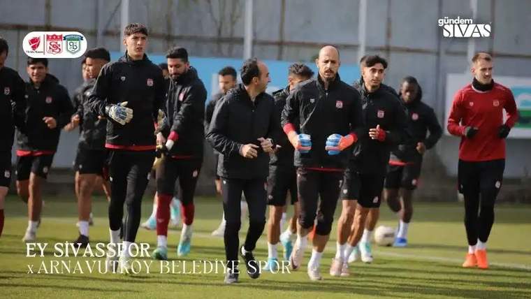 Antrenman sahasında koşan sporcuların önünde eldivenli bir kaleci, arkada takım arkadaşları görülüyor.