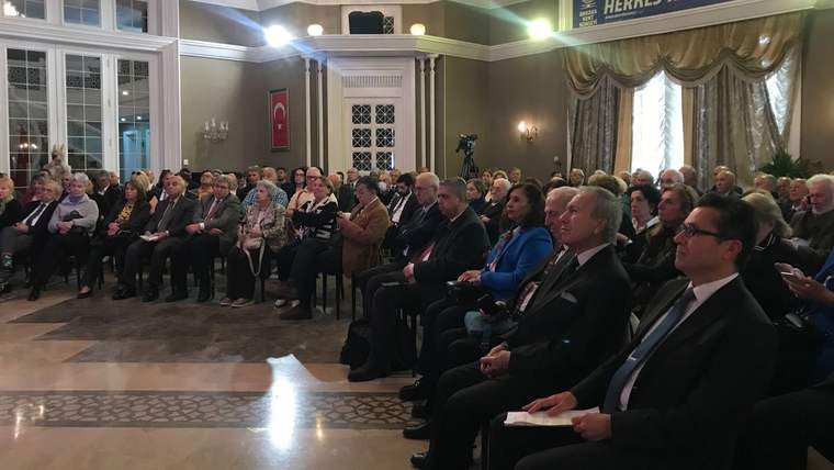 Türk bayrağının bulunduğu süslü salonda, sıralar halinde oturan kalabalık bir topluluk görülüyor.