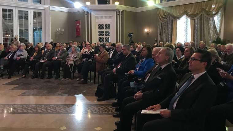 Türk bayrağının bulunduğu süslü salonda, sıralar halinde oturan kalabalık bir topluluk görülüyor.