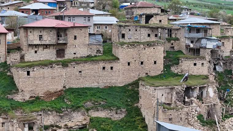 Yıkık taş yapılar ve yeşil alanlarla dolu bir köy manzarası.