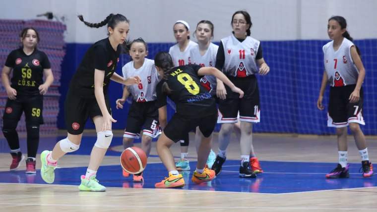 Spor salonunda kız basketbolcular, turuncu top için mücadele ederken bazı oyuncular pozisyon bekliyor.