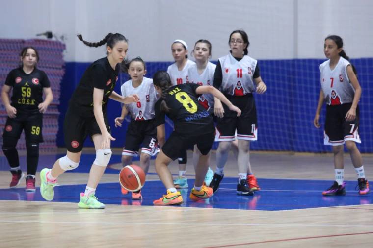 Spor salonunda kız basketbolcular, turuncu top için mücadele ederken bazı oyuncular pozisyon bekliyor.