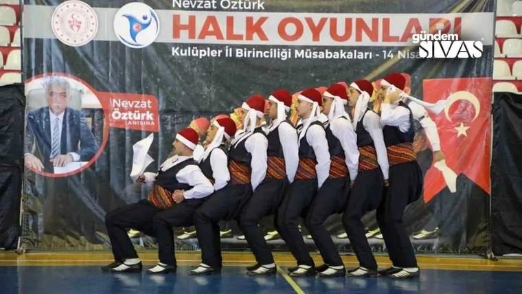 Geleneksel kıyafetler giyen bir halk oyunları ekibi, salonda senkronize adımlarla gösteri yapıyor.