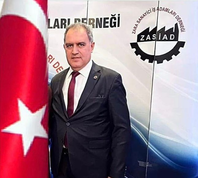 ZASİAD logosunun arkasında, takım elbise giymiş bir kişi, Türk bayrağının yanında duruyor.