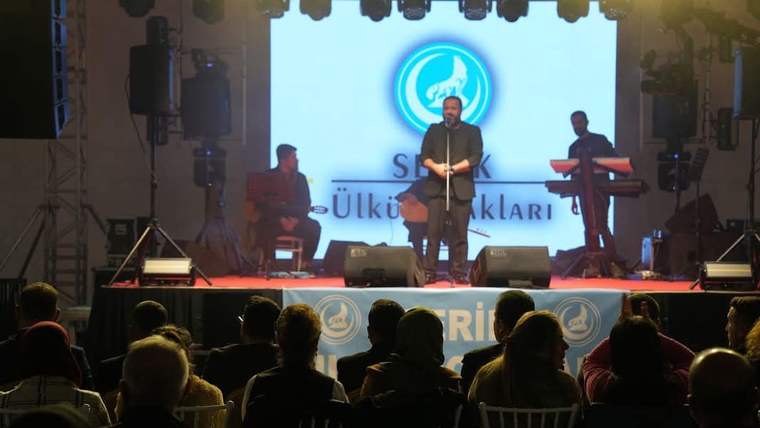 Bir sahnede mikrofonla şarkı söyleyen bir kişi, arka planda müzisyenler var.