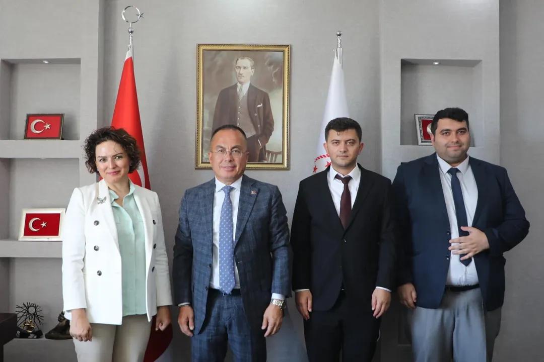 Atatürk portresi ve Türk bayraklarının önünde duran, takım elbiseli dört kişi görülüyor.
