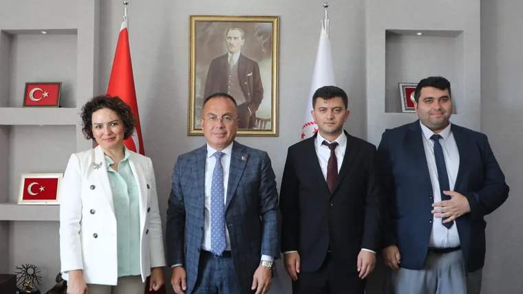 Atatürk portresi ve Türk bayraklarının önünde duran, takım elbiseli dört kişi görülüyor.