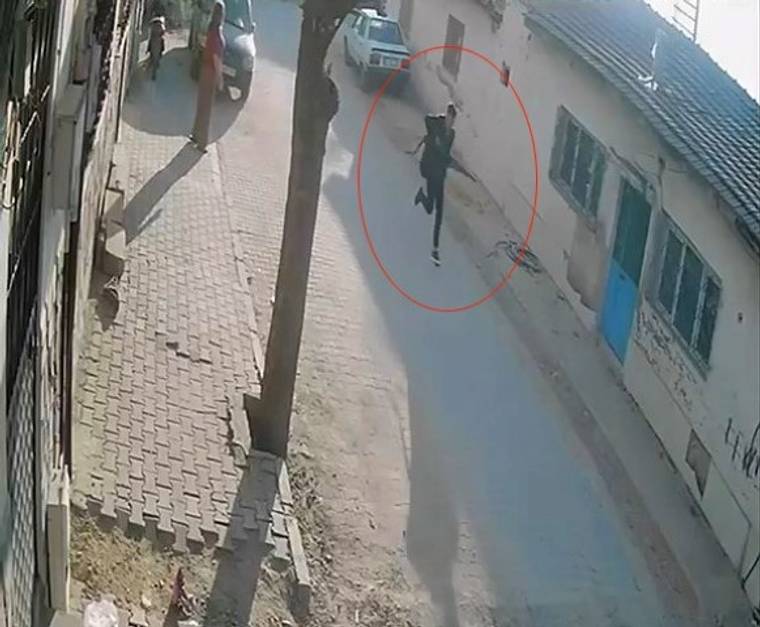 Güvenlik kamerası görüntüsünde, dar sokakta kırmızı çemberle işaretlenmiş bir kişi koşuyor.
