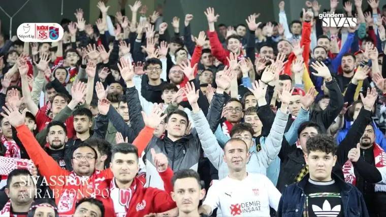 Stadyumda ellerini havaya kaldırmış kalabalık bir taraftar grubu.