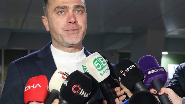 Koyu ceketli bir kişi, üzerinde DHA, İHA ve 58 Spor logoları bulunan mikrofonlara konuşuyor.