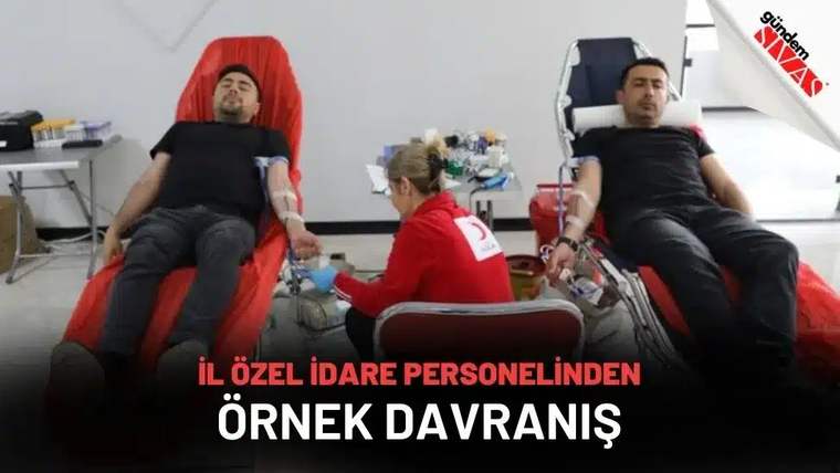 Kırmızı koltuklarda oturan iki erkekten sağlık görevlisi kan alırken, aralarında tıbbi malzemeler görülüyor.