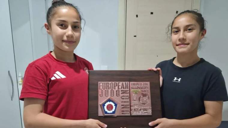 İki genç kız, ellerinde judo ödülüyle gülümsüyorlar.