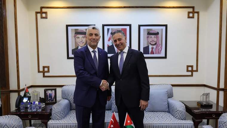 İki kişi, bir odada el sıkışarak poz veriyor; arka planda Türkiye ve Ürdün bayrakları var.