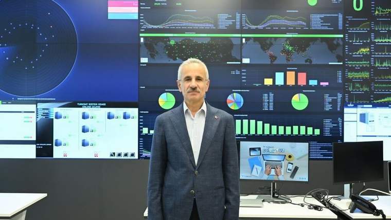 Takım elbiseli bir kişi, grafikler ve dünya haritalarının yer aldığı güvenlik ekranlarının önünde duruyor.